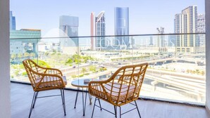 A balcony with two wicker chairs and a small table, overlooking a cityscape with modern buildings and a highway. - Bloomfields 1Br Supremee Al Maryah  (Abu Dhabi)