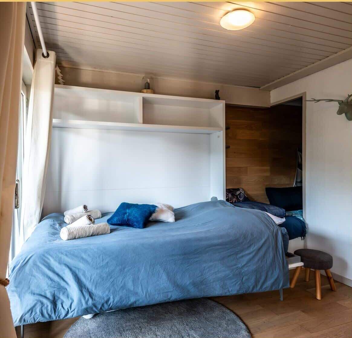 A bedroom with a bed, pillows, a small stool, and a nightstand.