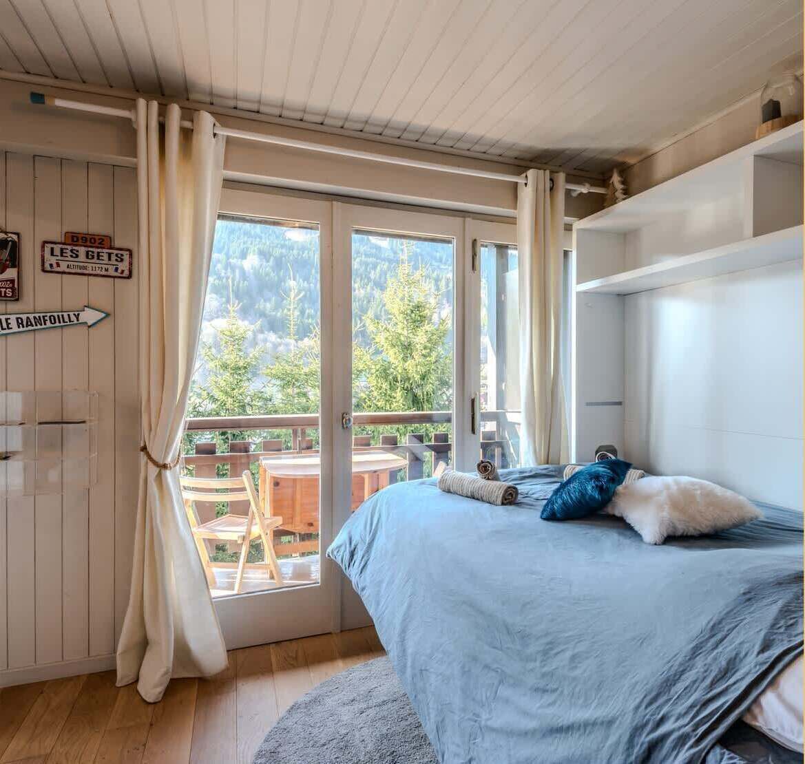 A bedroom with a bed, a window with curtains, a view of trees, and a sign on the wall.