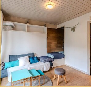 A cozy room with a sofa, a small table, and a bench. There is a wooden floor and a ceiling with wooden beams. - La Grange Neuve I T1 I Les Gets (Les Gets)