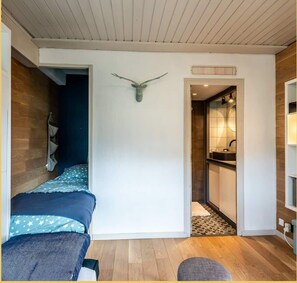 A bedroom with a bed, a wall-mounted deer head decoration, a wooden floor, and a bathroom visible through an open door. - La Grange Neuve I T1 I Les Gets (Les Gets)
