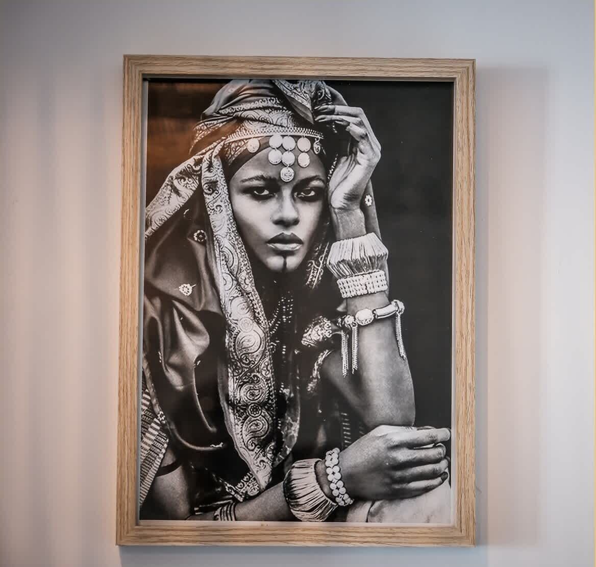 Fotografia in bianco e nero incorniciata, raffigurante una persona in abiti tradizionali con motivi elaborati e gioielli.
