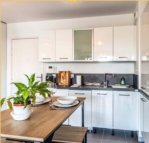 A modern kitchen with white cabinets, a wooden countertop, and a dining table set with plates and a glass.