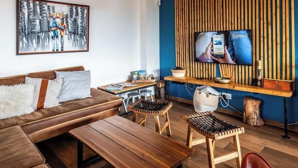 A living room with a brown sofa, wooden coffee table, two woven stools, a television on a wooden stand, and a painting on the wall. - Villa Amadieu · Détente, confort et sérénité, aux portes de Genève (Collonges)