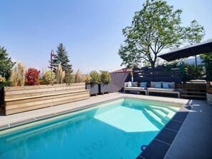 Une piscine avec des marches en bois et un espace détente doté de coussins.