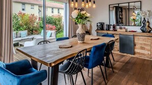A modern kitchen with a wooden table, blue chairs, and a hanging light fixture. - Villa Amadieu · Détente, confort et sérénité, aux portes de Genève (Collonges)