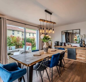 A modern kitchen with a wooden table, blue chairs, and a hanging light fixture.