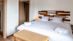 A hotel room with a large bed, wooden headboard, a bedside table with a lamp, and a hanging light fixture. - Villa Amadieu · Détente, confort et sérénité, aux portes de Genève (Collonges)
