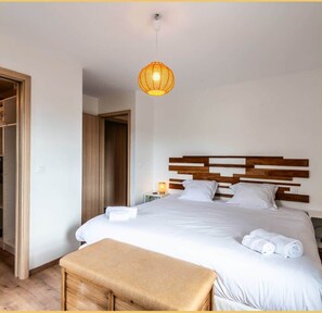A hotel room with a large bed, wooden headboard, a bedside table with a lamp, and a hanging light fixture.