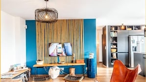 A modern living room with a TV, wooden furniture, and a kitchen in the background. - Villa Amadieu · Détente, confort et sérénité, aux portes de Genève (Collonges)