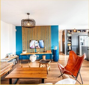 A modern living room with a TV, wooden furniture, and a kitchen in the background.