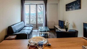 A modern living room with a leather sofa, a glass dining table set with plates, glasses, and cutlery, and a television on a stand. - Chez Dams I T2 I Annecy (Annecy)