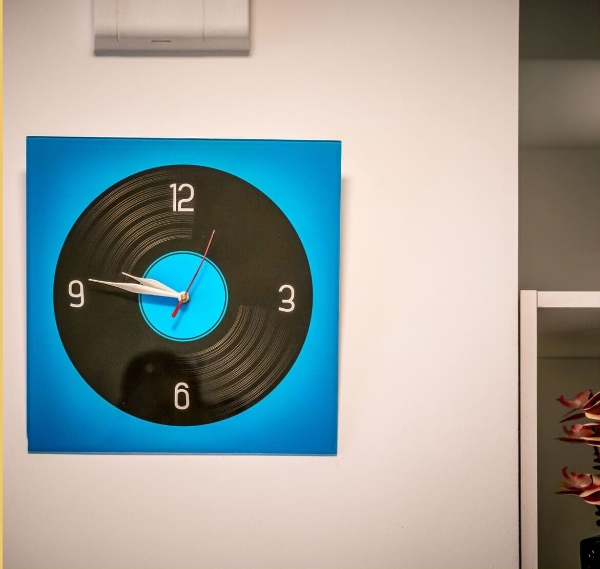 Een wandklok met een blauwe achtergrond en een zwarte ronde wijzerplaat.
