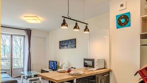 A modern kitchen with a dining area, a flat-screen TV, a microwave, and a red induction cooktop. - Chez Dams I T2 I Annecy (Annecy)