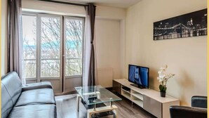 A modern living room with a glass coffee table, leather sofa, and a TV on a stand. - Chez Dams I T2 I Annecy (Annecy)