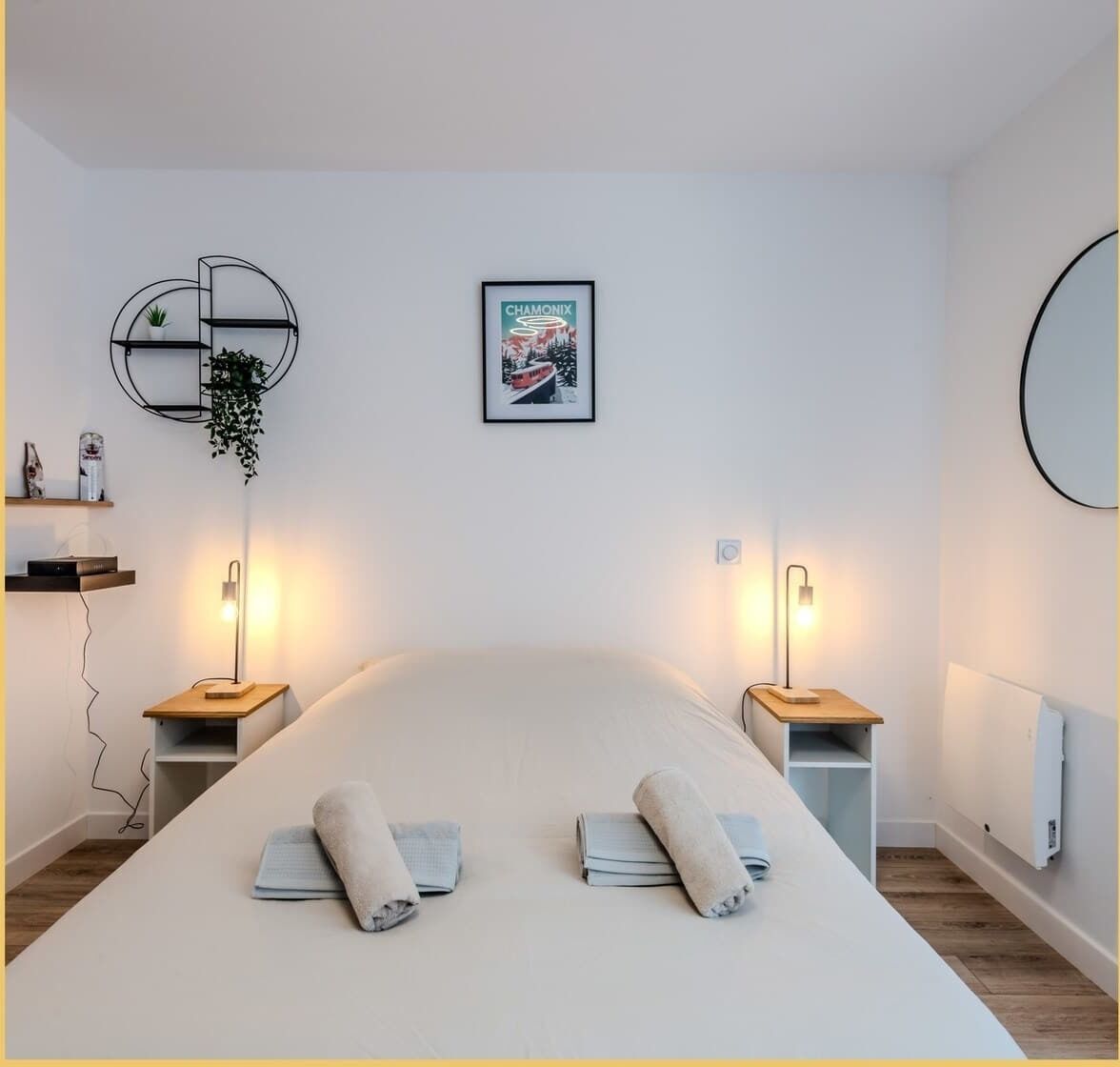 A modern bedroom with a large bed, two bedside tables with lamps, a wall-mounted shelf with a plant, and a framed picture.