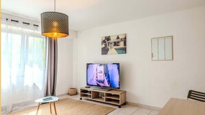 A modern living room with a flat-screen TV, a dining table, and a large window with curtains.