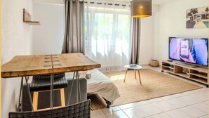 A modern living room with a wooden table, a sofa, a TV, and a hanging lamp.