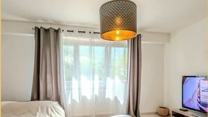 A bedroom with a bed, a small round table, a television, and a hanging lamp.