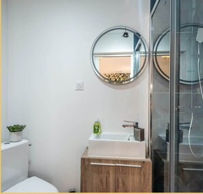 A modern bathroom with a toilet, a sink with a mirror above it, and a glass shower enclosure. - Chez Carole I Studio I Annemasse (Annemasse)