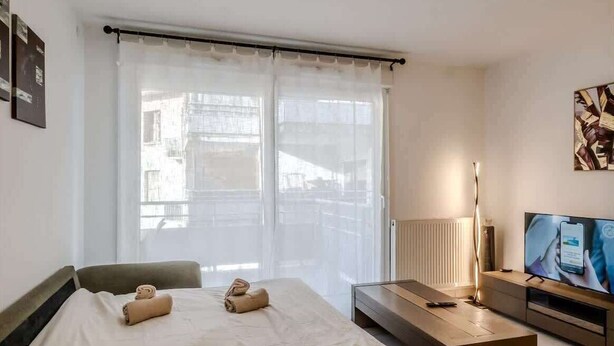 A hotel room with a bed, a TV, a desk, and a window with curtains. - Le Manoir de Jérémy I T2 I Thonon (Thonon-les-Bains)