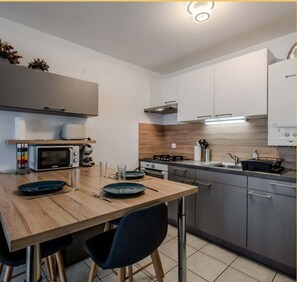 Une cuisine moderne avec une table à manger en bois, deux chaises, un four à micro-ondes, une cuisinière et un évier.
