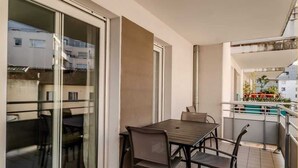 A balcony with a table and chairs, a sliding glass door, and a view of neighboring buildings. - Le Manoir de Jérémy I T2 I Thonon (Thonon-les-Bains)