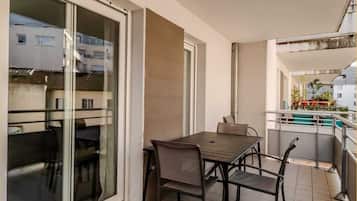 Ein Balkon mit Tisch und Stühlen, eine Glastür und Blick auf umliegende Gebäude.
