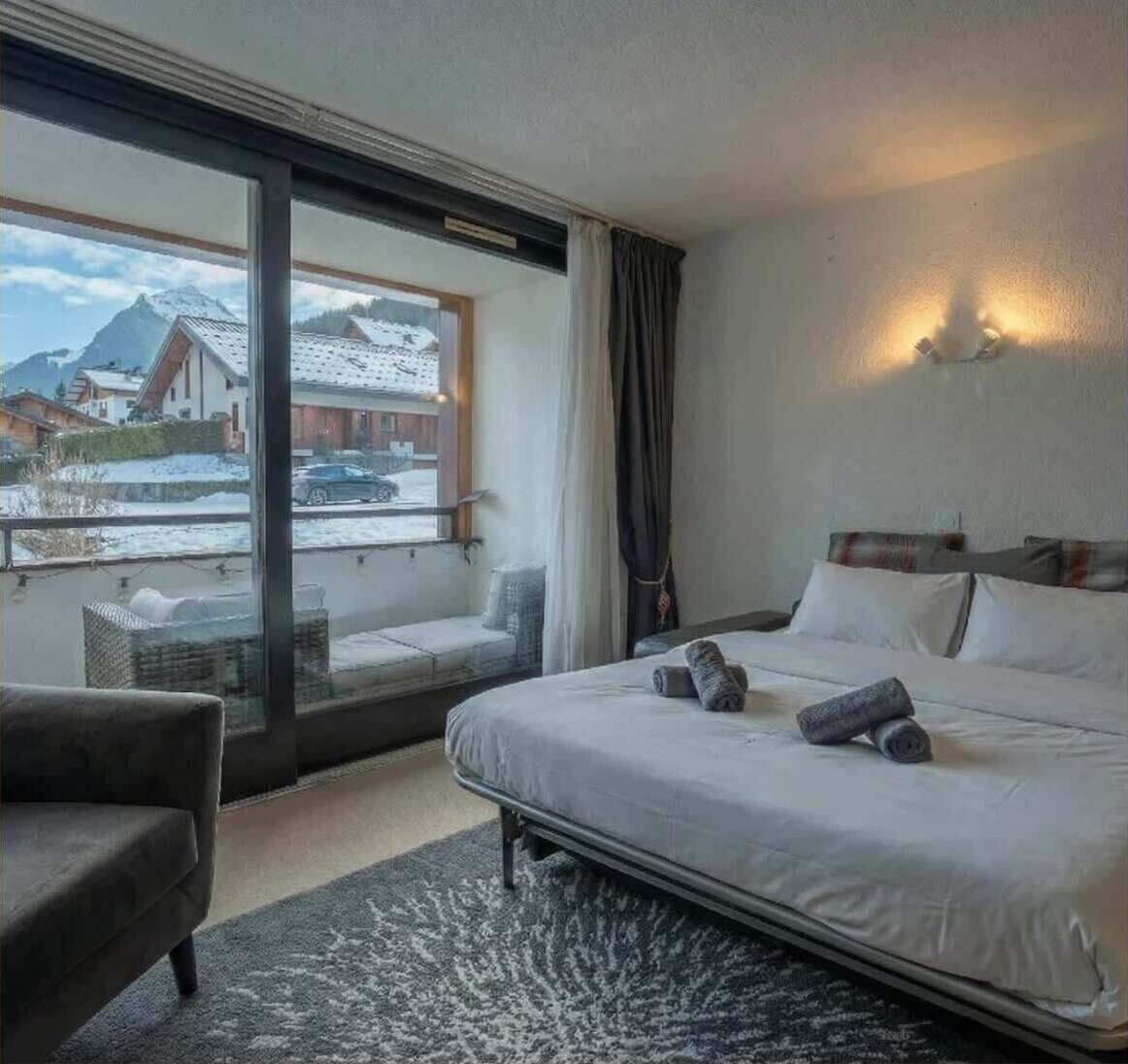 Habitació d'hotel amb un llit gran, un sofà i un balcó que dona a les muntanyes cobertes de neu.