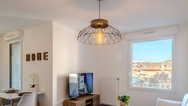 A modern hotel room with a large bed, a desk with a chair, a television, and a large window offering a city view. - Le Dessaix I Studio I Thonon (Thonon-les-Bains)