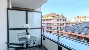 A balcony with a table and chairs, a potted plant, and a view of surrounding buildings. - Le Dessaix I Studio I Thonon (Thonon-les-Bains)