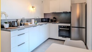 A modern kitchen with white cabinets, a stainless steel refrigerator, a microwave, and a built-in oven. - Le Dessaix I Studio I Thonon (Thonon-les-Bains)