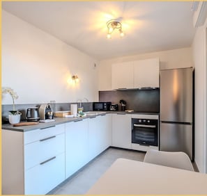 Eine moderne Küche mit weißen Schränken, einem Edelstahlkühlschrank, einer Mikrowelle und einem eingebauten Backofen.