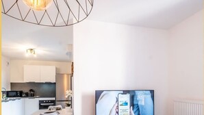 A modern living room with a flat-screen TV, wooden entertainment unit, and a dining area with a white table and chairs. - Le Dessaix I Studio I Thonon (Thonon-les-Bains)