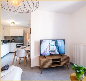 Ein modernes Wohnzimmer mit Flachbildfernseher, einer Holzunterhaltungsecke und einem Essbereich mit weißem Tisch und Stühlen.