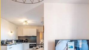 A modern living room with a TV, a wooden entertainment unit, and a dining area with a table and chairs. - Le Dessaix I Studio I Thonon (Thonon-les-Bains)