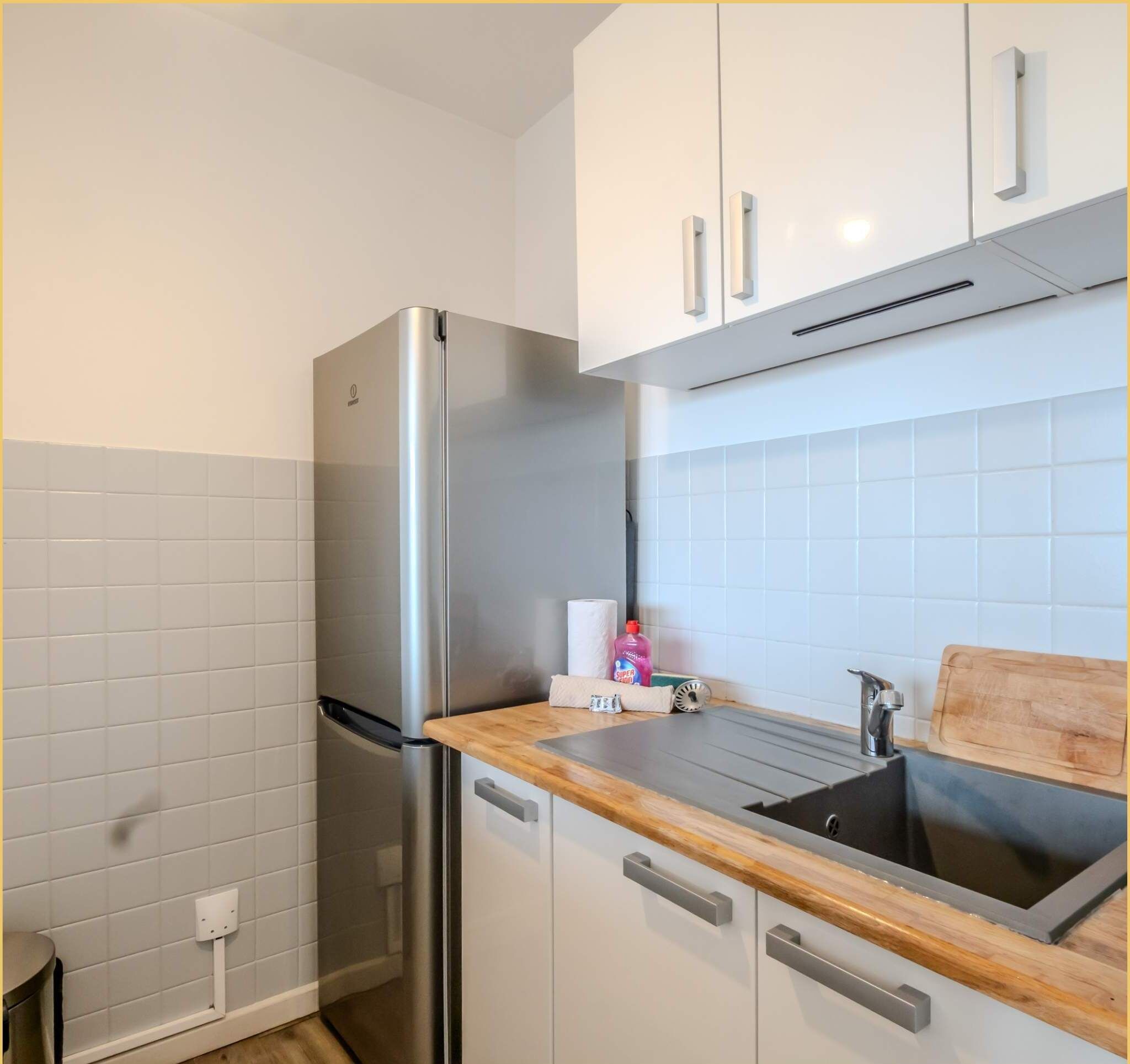Una cocina moderna con armarios blancos, un refrigerador de acero inoxidable, una encimera de madera y un lavamanos.