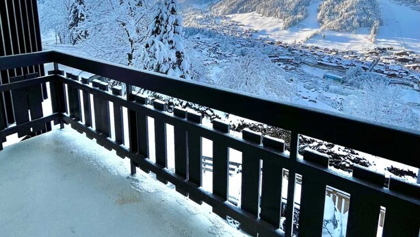 En balkon med udsigt over et sneklædt landskab, inklusive træer og fjerne bjerge.