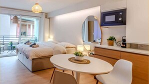 Et moderne soveværelse med seng, sengeborde, et rundt spisebord med stole, et tekøkken med mikroovn, samt en balkon med bord og stole.