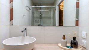 Et moderne badeværelse med en stor, hvid vask, en brusekabine med glasvægge og et spejl over vasken.