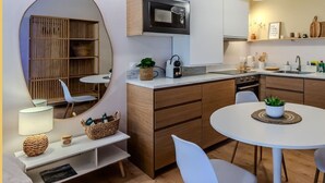 Et moderne køkken med mikrobølgeovn, vask og spiseområde. Der er et rundt bord med stole og en lille plante på bordet.