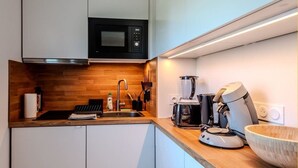 Une cuisine moderne avec des meubles blancs, un micro-ondes noir, une machine à café et un plan de travail en bois.