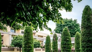 Ein Weg, gesäumt von ordentlich geschnittenen Formschnitten und kugelförmigen Steinbildwerken in einer angelegten Gartenanlage.
