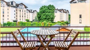 Ein Balkon mit Holztisch und Stühlen, mit Blick auf einen Swimmingpool und eine Reihe von Wohngebäuden.