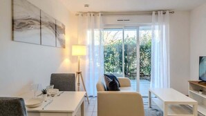 Een moderne woonkamer met een eethoek, een bank, een televisie en een groot raam met gordijnen.