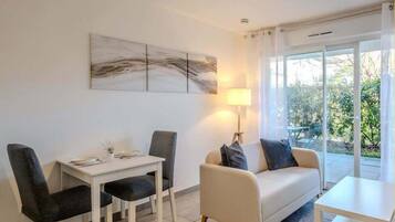 Ein modernes Wohnzimmer mit einer Couch, einem Esstisch mit Stühlen und einem großen Fenster mit Blick auf Grünflächen.