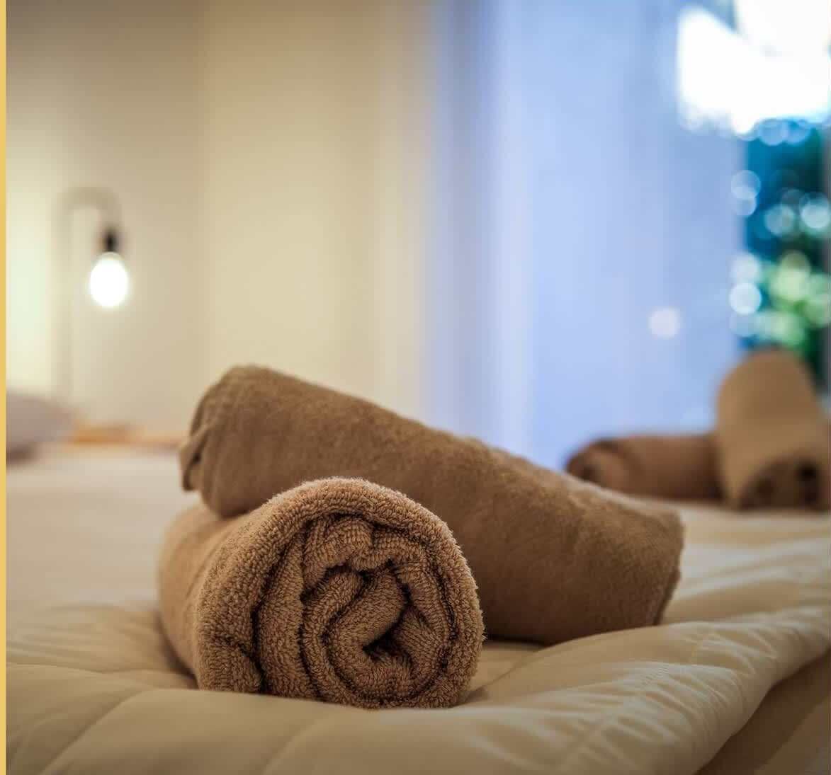 A neatly made bed with rolled towels and a visible light fixture on the wall.