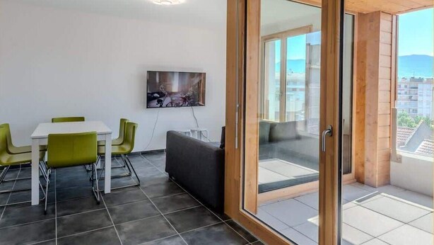 Ein modernes Wohnzimmer mit Essbereich, eine große Schiebeglas-Tür, die auf einen Außenbalkon führt, und ein an der Wand befestigtes Kunstwerk.