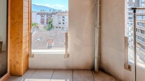 Ein Balkon mit Holzboden, einer Betonwand und Blick auf eine Stadtansicht.