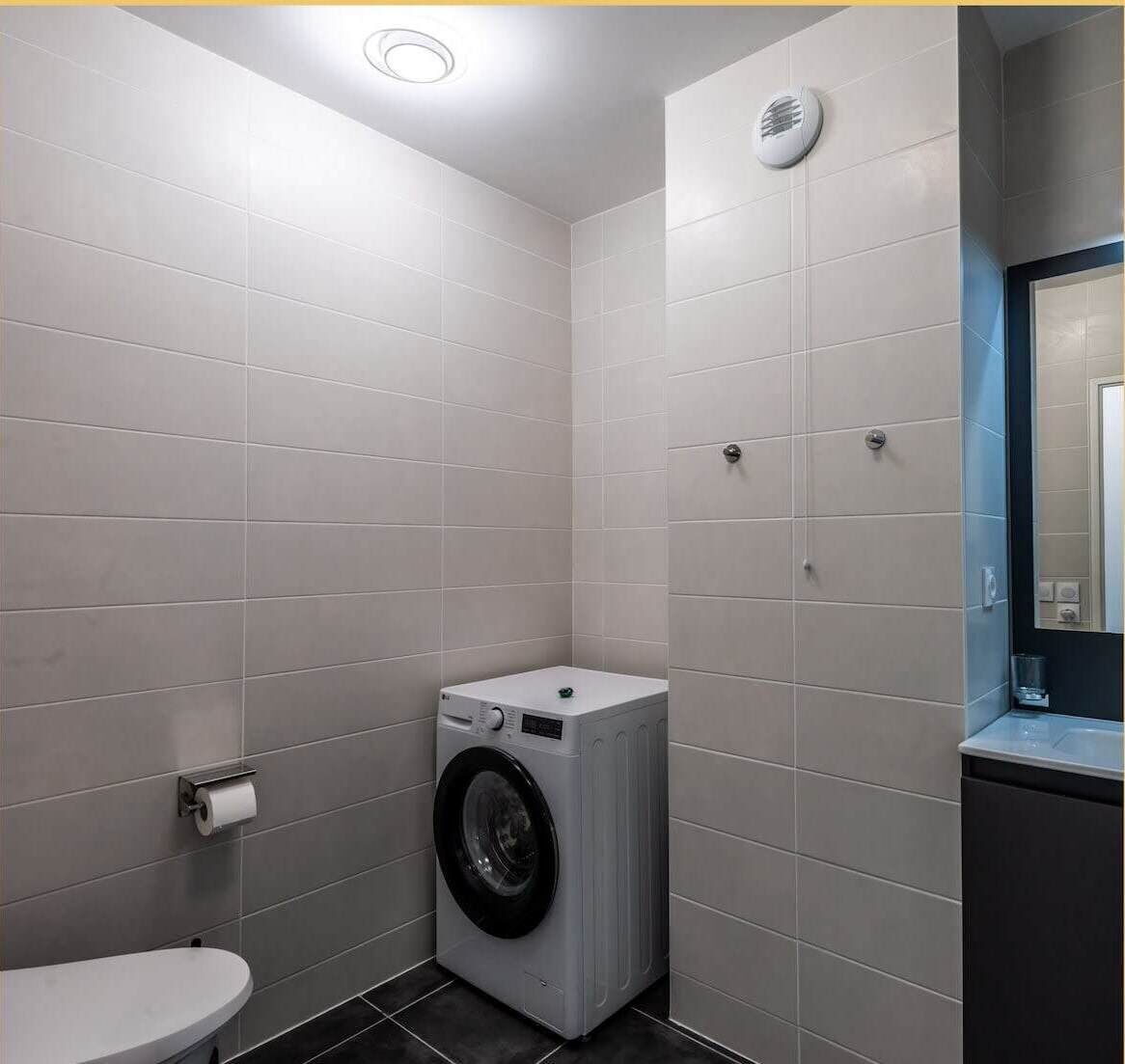 A compact laundry room with a washing machine, a toilet, and a small sink.